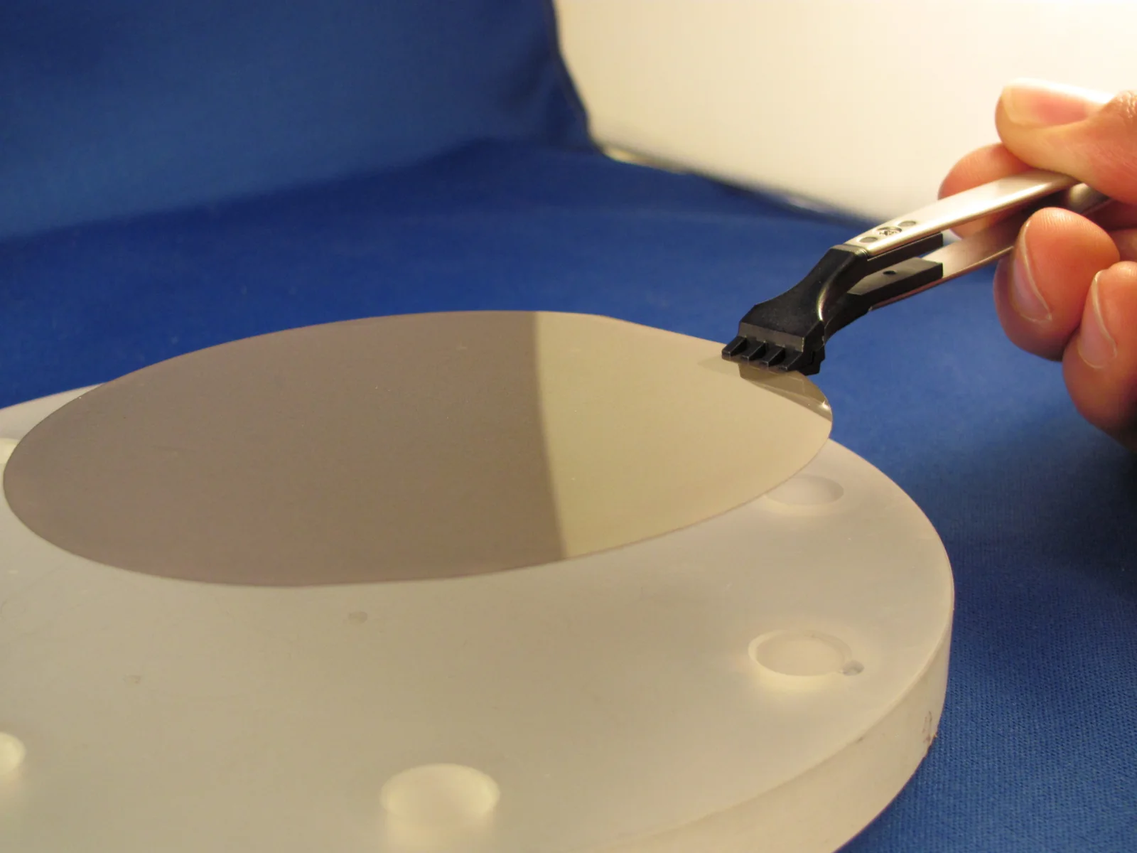 A polished CVD polycrystalline diamond disc lifted from its holder with tweezers